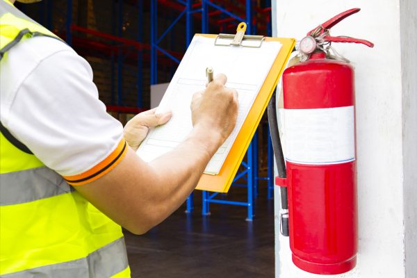 Engineer technician checking fire extinguisher writing on clipboard at warehouse. Inspection Fire protection inside the building.